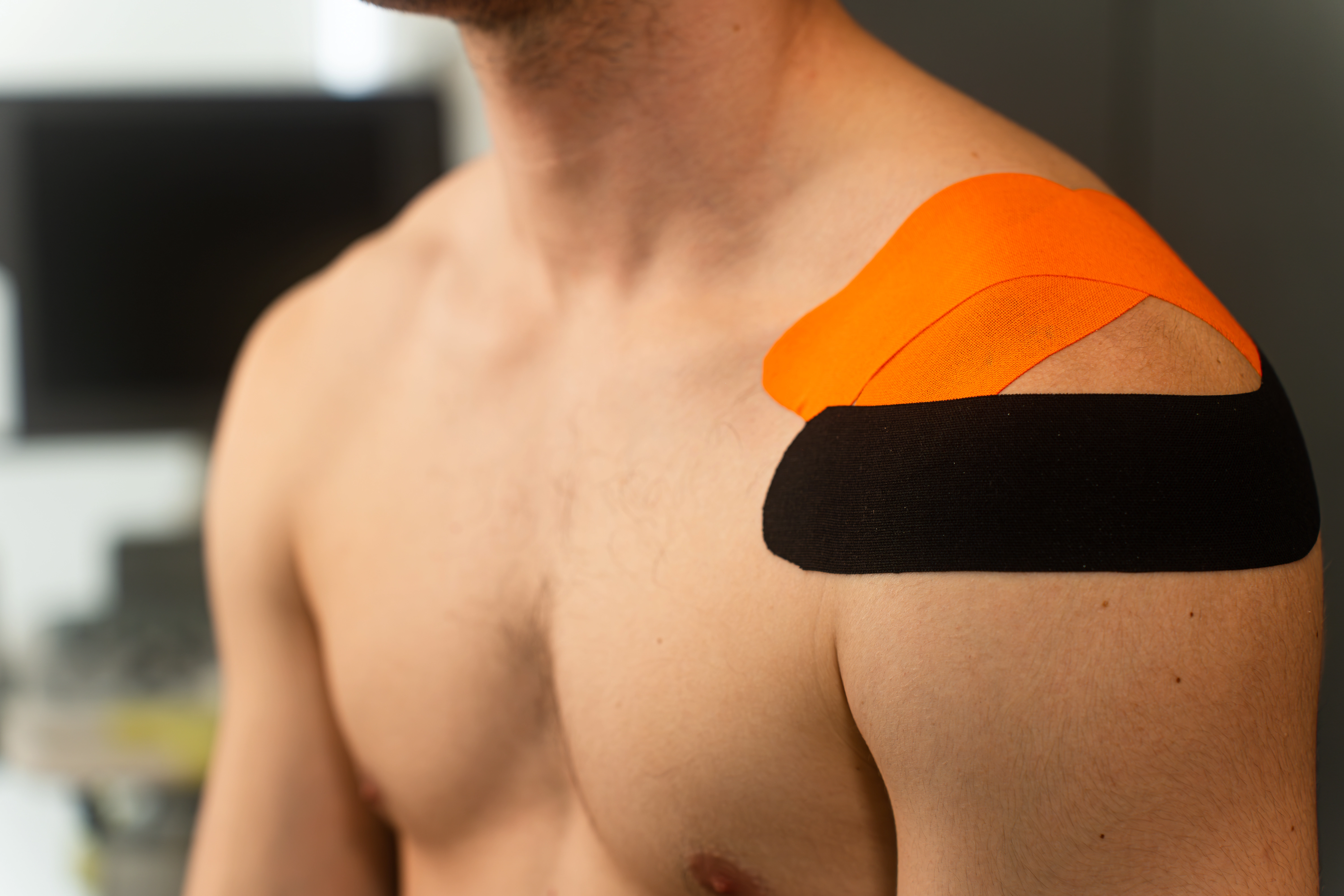 Aplicación de kinesiotape naranja y negro en hombro masculino para estabilización articular
